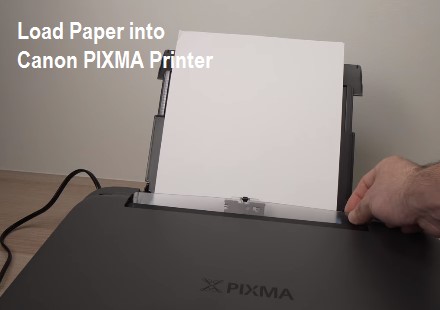 A close-up image of a hand loading a stack of white paper into a Canon PIXMA printer tray.